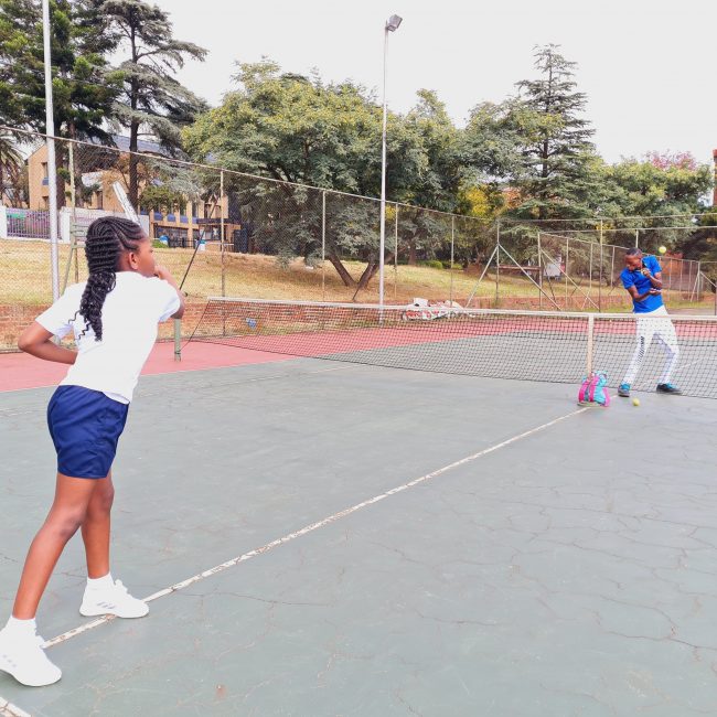a student from amazing grace private school playing tennis with her trainer
